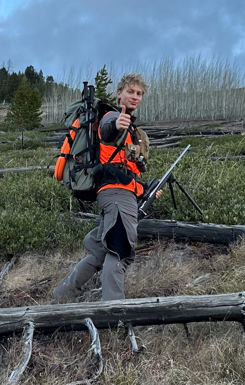 Mason Eacker-Rude in hunting gear giving a thumbs up in a burned forest clearing