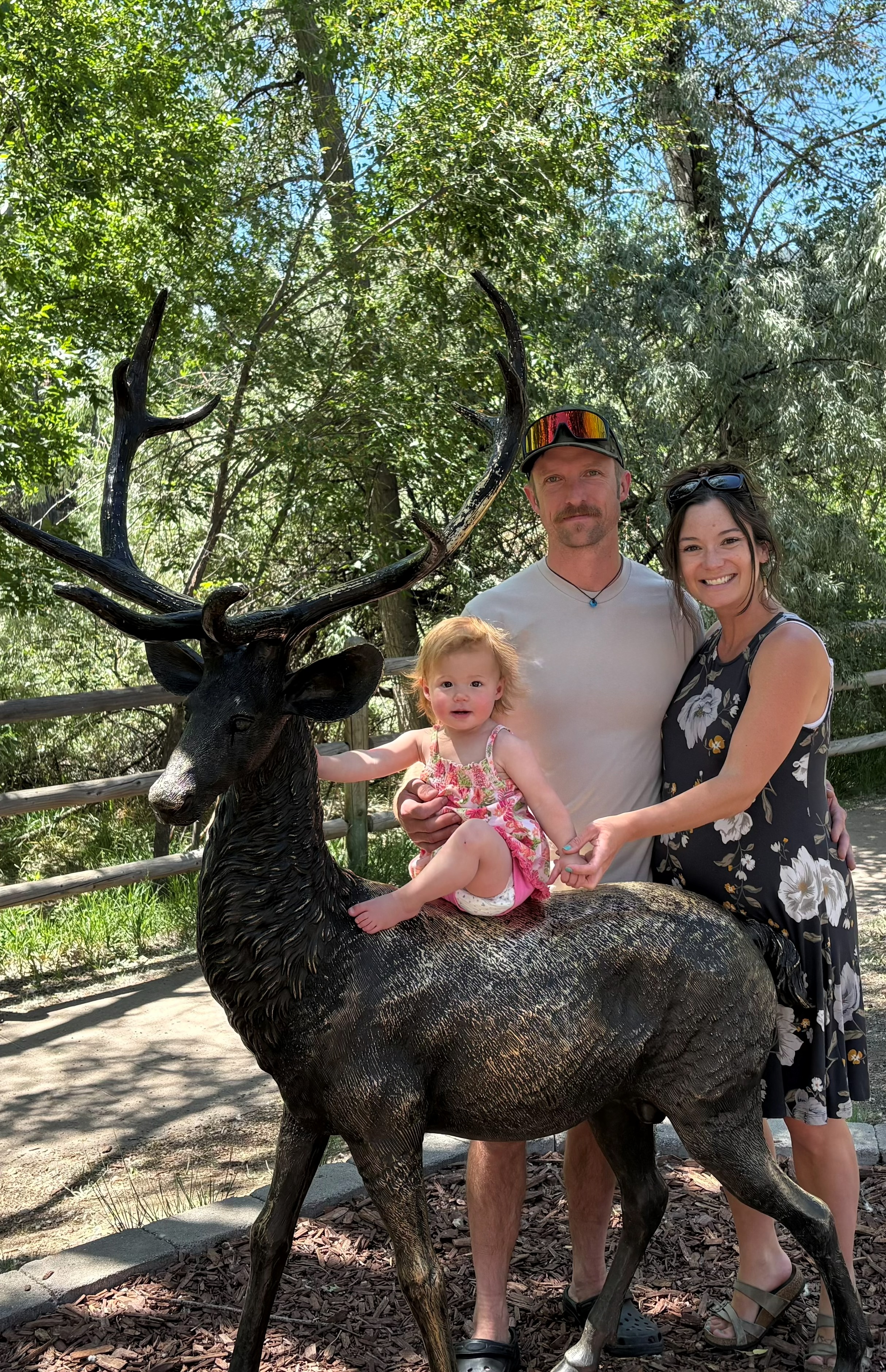 Nick Prendergrast outdoors with family beside a large bronze deer statue on a sunny day
