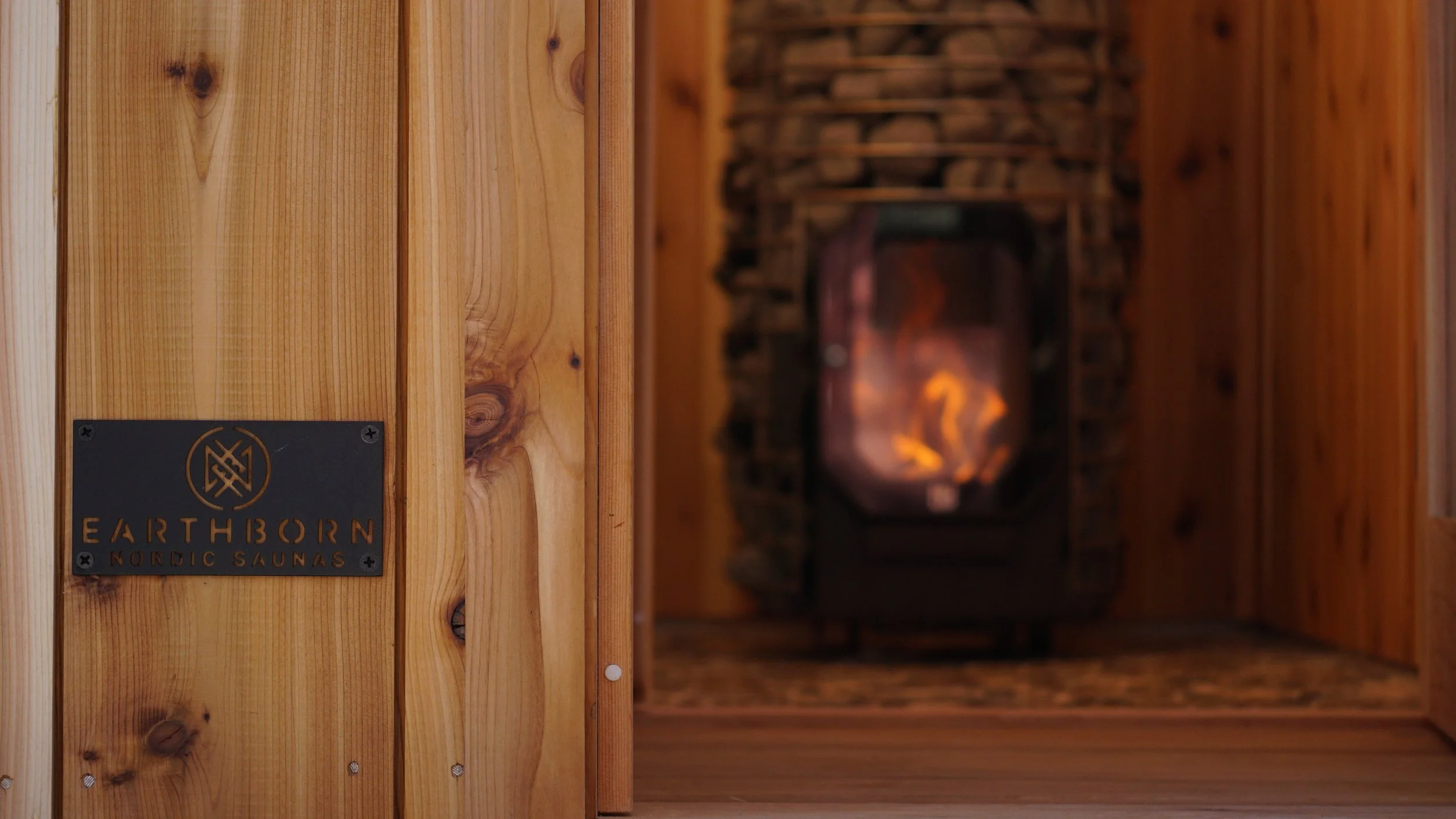 Close-up of a maker's plate mounted on a cedar door, with a wood-fired heater glowing in the background