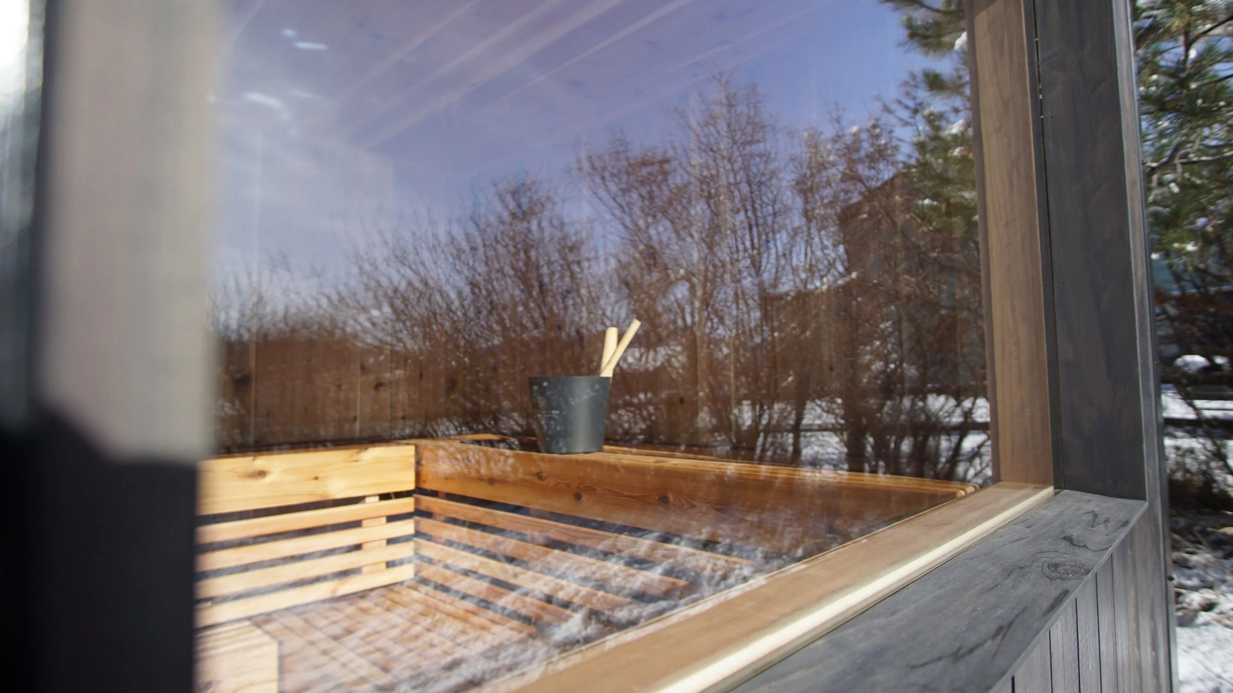 Sauna bucket and ladle on a cedar bench, seen through the sauna's large window